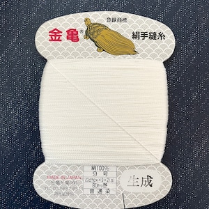May include: A spool of white silk thread with a label that reads "絹100% 9号 23dtex×9×2(s) 80m巻 普通染 生成" in Japanese. The label also includes the text "MADE IN JAPAN 金亀糸業(株) TEL 03-5687-8511 生徒紙使用" in Japanese.