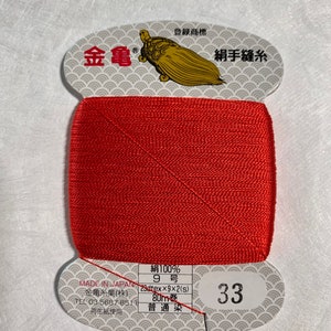 May include: A spool of red silk thread for hand sewing. The label reads "Silk 100%, 9 Gauge, 29dtex x 9 x 2(s), 80m, Ordinary Dye, 33". The label also has a gold turtle logo and the text "Kin-Kame, Silk Hand Sewing Thread".