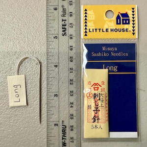 Pu&ograve; includere: Un pacchetto di aghi sashiko lunghi di Misuya, etichettato "Long" e "5本入" (5 pezzi). Il pacchetto &egrave; su uno sfondo blu con un bordo bianco e le parole "Little House" in lettere bianche.