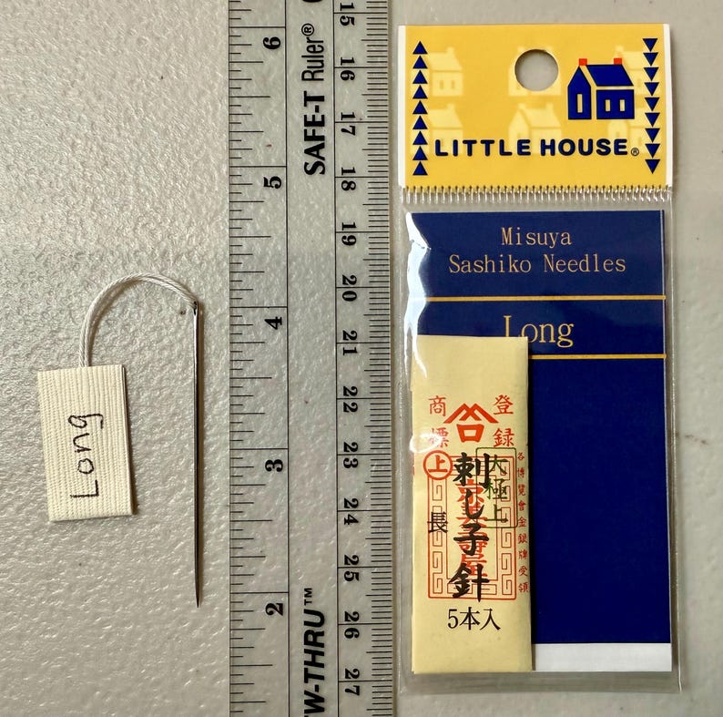Pu&ograve; includere: Un pacchetto di aghi sashiko lunghi di Misuya, etichettato "Long" e "5本入" (5 pezzi). Il pacchetto &egrave; su uno sfondo blu con un bordo bianco e le parole "Little House" in lettere bianche.