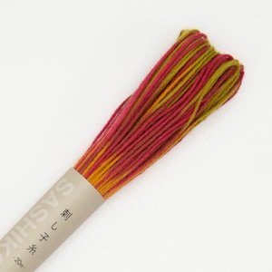 May include: A skein of embroidery floss in shades of red, orange, and green. The floss is wound around a cardboard spool with the text "Sashiko 刺し子" and "型  こし" printed on it.