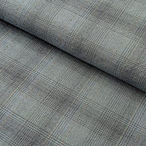 May include: Close-up of a folded fabric with a plaid pattern. The fabric is primarily light blue-gray with a grid of black lines and small, scattered orange-brown stitches. The texture appears slightly textured.