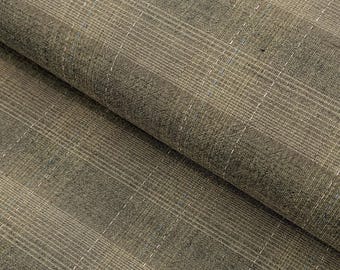 May include: Close-up of a folded fabric with a plaid pattern. The fabric is a blend of tan, brown, and gray hues, with thin white and blue lines creating the plaid design. The texture appears soft and slightly textured, suitable for apparel or home decor.