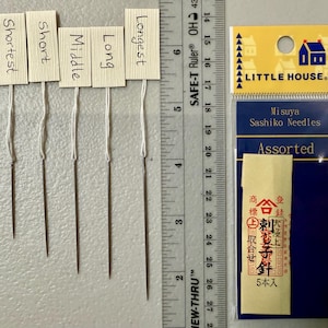 Pu&ograve; includere: Cinque aghi per sashiko di diverse lunghezze, etichettati "Shortest", "Short", "Middle", "Long" e "Longest". Gli aghi sono confezionati in un sacchetto di plastica trasparente con un'etichetta blu e bianca che recita "Misuya Sashiko Needles Assorted" e presenta una piccola icona di casa. L'etichetta include anche testo giapponese.