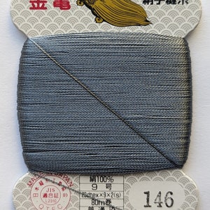 May include: A spool of gray silk thread with a label that reads "絹100% 9号 20dtex×9×2(s) 80m巻 普通染 金亀糸業(株) TEL 03-5687-8511" and "絹手縫糸 146".