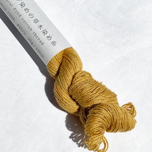 May include: A skein of natural dyed cotton thread in a mustard yellow color. The label reads "Natural dyed cotton thread #10/2 16g/160m" in Japanese and English.