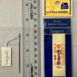 Pu&ograve; includere: Un pacchetto di aghi Sashiko Misuya etichettato "Longest". La confezione &egrave; gialla con testo nero e un sigillo rosso. Gli aghi sono esposti su una carta bianca con il testo "Longest" scritto su di essa.