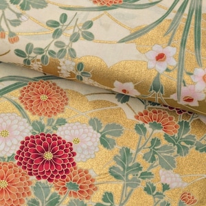 May include: A fabric featuring a repeating pattern of orange, red, and white chrysanthemum flowers with green leaves. The background is a cream color with metallic gold wave-like accents and thin gold lines throughout the floral design.