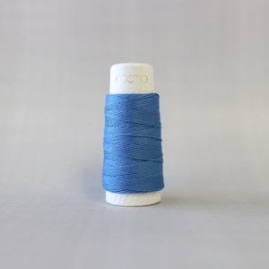 May include: A spool of blue thread on a white bobbin with the word "cosmo" printed on the bobbin.