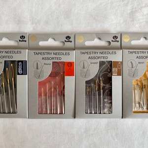 May include: Four packages of Tulip tapestry needles, each with a different needle type: round, sharp, bent, and assorted. The packages are white with a gray border and feature a small Tulip logo.