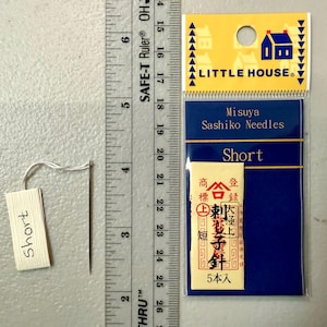 Pu&ograve; includere: Un pacchetto di aghi sashiko corti di Misuya, etichettato "Little House" e "Short". La confezione &egrave; blu con lettere bianche e una piccola illustrazione di una casa. Gli aghi sono confezionati in una piccola busta bianca con testo giapponese.