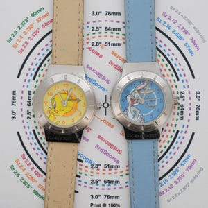May include: Two Looney Tunes character watches. One watch has a yellow face with Tweety Bird, the other has a blue face with Bugs Bunny. Both watches have silver-tone cases and fabric bands.