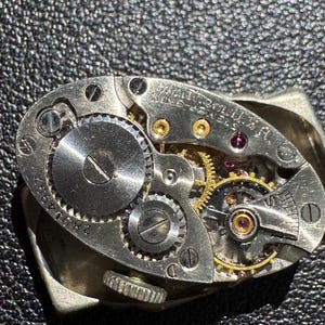 Op de afbeelding: Close-up van een zilveren uurwerk met zichtbare tandwielen en schroeven. Het uurwerk is gemarkeerd met "WALTHAM 17 JEWELS 16 SIZE".