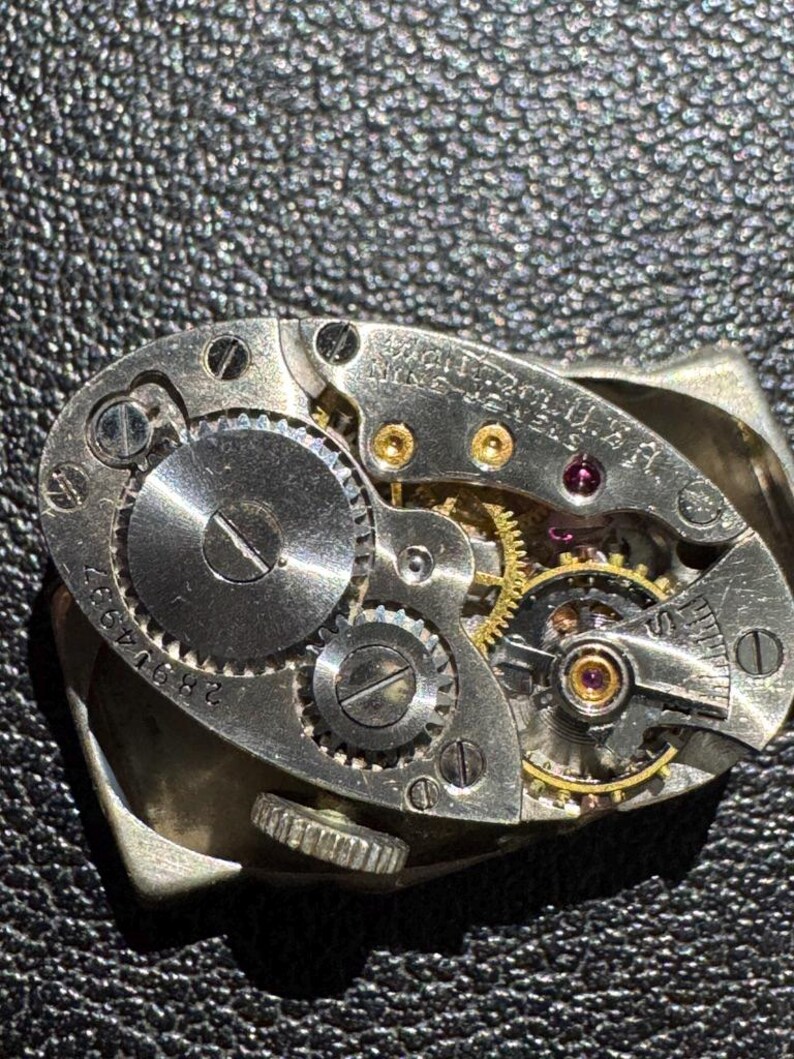 Op de afbeelding: Close-up van een zilveren uurwerk met zichtbare tandwielen en schroeven. Het uurwerk is gemarkeerd met "WALTHAM 17 JEWELS 16 SIZE".