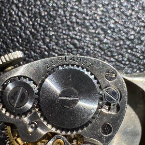 Op de afbeelding: Close-up van een zilveren uurwerkmechanisme met zichtbare tandwielen en de gegraveerde nummers 2891 4997 op de buitenring.