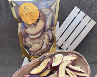 May include: A bag of freeze-dried peach slices. The bag is gold with a white label that says "Rk Freeze Dried Goodies Peach Slices Keep It Zipped Keep It Crisp". The peach slices are in a wooden bowl.
