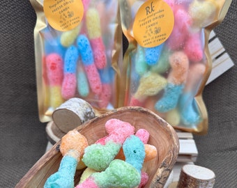 Può includere: Una ciotola di caramelle liofilizzate colorate a forma di vermi. Le caramelle sono in una ciotola di legno e sono circondate da fette di legno. Le caramelle sono in un sacchetto con la scritta "Freeze Dried Candy" sopra.
