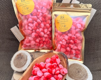 Può includere: Due sacchetti dorati richiudibili pieni di caramelle liofilizzate. Le caramelle sono rosa e bianche e hanno la forma di piccoli cuori. I sacchetti hanno un'etichetta che dice "Freeze dried goodies FREEZE DRIED CANDY KEEP IT ZIPPED KEEP IT CRISP". Una ciotola di legno piena delle stesse caramelle è in primo piano.