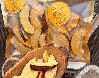 May include: Two clear plastic bags filled with dried nectarine slices. The bags are gold and have a label that says "Rk Freeze dried goodies ORGANIC NECTARINE SLICES KEEP IT ZIPPED KEEP IT CRISP". A wooden bowl filled with dried nectarine slices sits on a wooden surface.