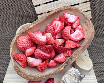 Op de afbeelding: Een houten kom gevuld met gesneden rode aardbeien. De kom staat op een houten oppervlak met een stuk berkenbast en een klein houten blokje.