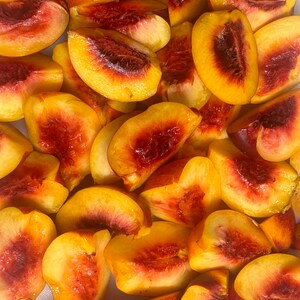 May include: A close-up of a white surface with many slices of fresh peaches. The peaches are cut into wedges and have a bright yellow and red color.