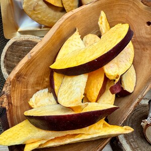 May include: A wooden bowl filled with dried peach slices. The peach slices are a light yellow color with some red and purple hues. The slices are arranged in a pile, with some overlapping.