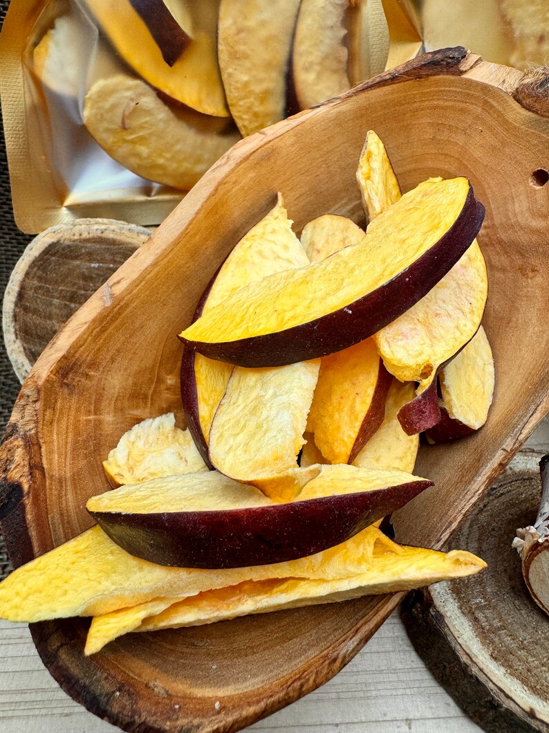 May include: A wooden bowl filled with dried peach slices. The peach slices are a light yellow color with some red and purple hues. The slices are arranged in a pile, with some overlapping.