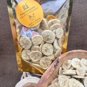 May include: A gold resealable bag filled with freeze-dried organic banana slices. The bag has a yellow label with the text "Rk Freeze dried goodies ORGANIC BANANAS KEEP IT ZIPPED KEEP IT CRISP".