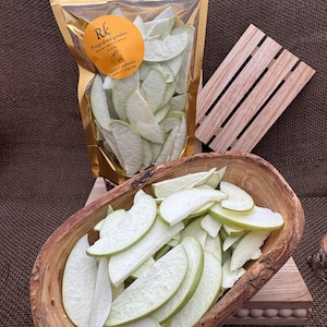 May include: A bag of dried Granny Smith apple slices in a wooden bowl. The bag has a label that says "Rk Freeze dried goodies Granny & Smith Apple Slices Keep it zipped Keep it crisp".