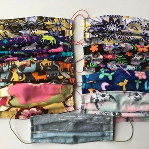 Op de afbeelding: Een verzameling van tien kleurrijke stoffen mondmaskers met verschillende patronen, waaronder bloemen, dieren en geometrische ontwerpen. De maskers zijn allemaal gevouwen en hebben elastische oorlussen.