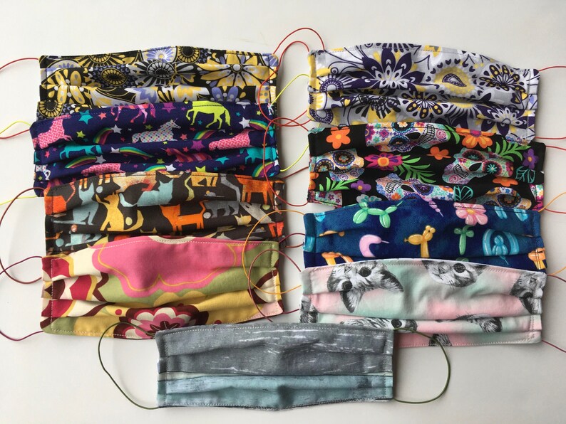 Op de afbeelding: Een verzameling van tien kleurrijke stoffen mondmaskers met verschillende patronen, waaronder bloemen, dieren en geometrische ontwerpen. De maskers zijn allemaal gevouwen en hebben elastische oorlussen.