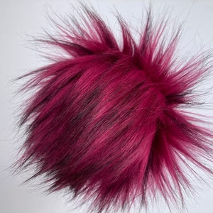 May include: A deep burgundy faux fur pom pom with black tips. The fur is soft and fluffy.