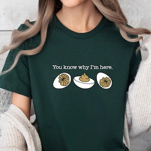 May include: Dark green t-shirt with the text "You know why I'm here." and a graphic of three deviled eggs. The graphic includes two halves of eggs with a filling and one egg with filling in a white bowl.
