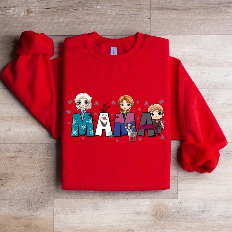 Puede incluir: Sudadera roja con un gr&aacute;fico de los personajes de Frozen, incluyendo Elsa, Anna, Olaf y Kristoff, deletreando la palabra "MAMA" con copos de nieve.