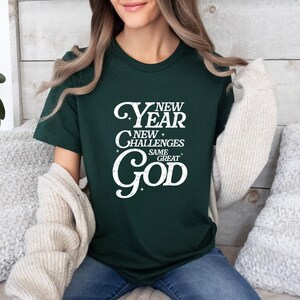 May include: A dark green t-shirt with a white graphic that reads "New Year New Challenges Same Great God".