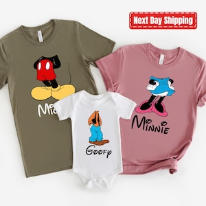 May include: Three t-shirts featuring cartoon characters from Disney. The first shirt is olive green with Mickey Mouse, the second shirt is pink with Minnie Mouse, and the third shirt is white with Goofy.