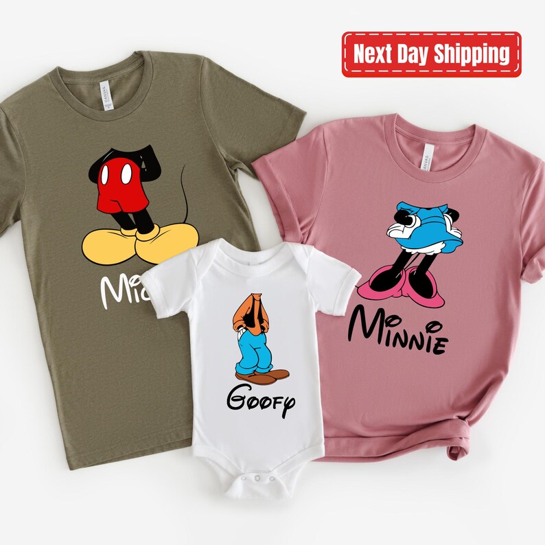 May include: Three t-shirts featuring cartoon characters from Disney. The first shirt is olive green with Mickey Mouse, the second shirt is pink with Minnie Mouse, and the third shirt is white with Goofy.
