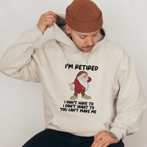 May include: A beige hooded sweatshirt with the text "I'M RETIRED" and a cartoon image of a dwarf. Below the image are the words "I DON'T HAVE TO I DON'T WANT TO YOU CAN'T MAKE ME".