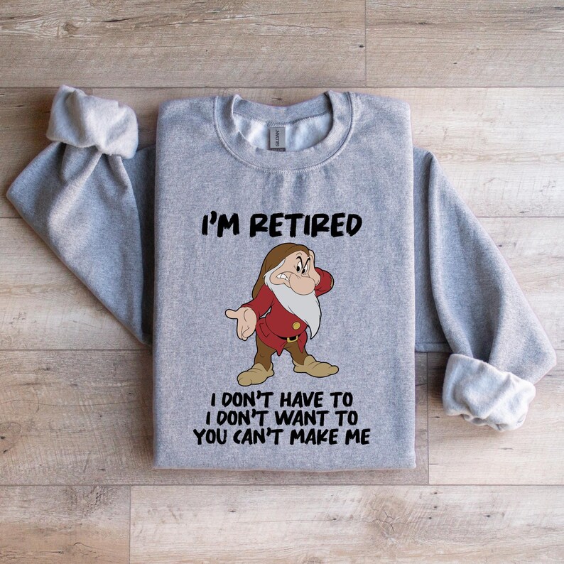 May include: A light gray sweatshirt with the text "I'M RETIRED" above a cartoon image of a dwarf character. Below the image, the text reads "I DON'T HAVE TO I DON'T WANT TO YOU CAN'T MAKE ME". The sleeves are cuffed.