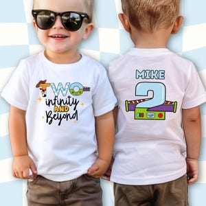 May include: White t-shirts with a colorful graphic design. The front of the shirt says "Two infinity and Beyond" with a cartoon cowboy hat and space ship. The back of the shirt has the name "Mike" and the number "2".