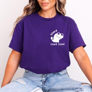 May include: A purple t-shirt featuring a white cartoon lizard graphic. The text "Lizard Lizard" is printed below the lizard illustration. The shirt is a solid color and has a crew neck.