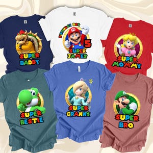 May include: A collection of six t-shirts in various colours featuring Super Mario character graphics. Each shirt displays a circular emblem with a character, including Mario, Bowser, Princess Peach, Yoshi, Rosalina, and Luigi, with custom text below.