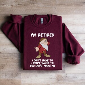 May include: A maroon sweatshirt with the text "I'M RETIRED" above a cartoon image of a dwarf. Below the image, the text reads "I DON'T HAVE TO I DON'T WANT TO YOU CAN'T MAKE ME".