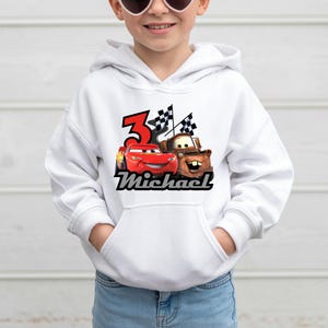May include: White hooded sweatshirt with a Cars movie design featuring Lightning McQueen and Mater, the number 3, and the name "Michael". The graphic includes checkered flags.