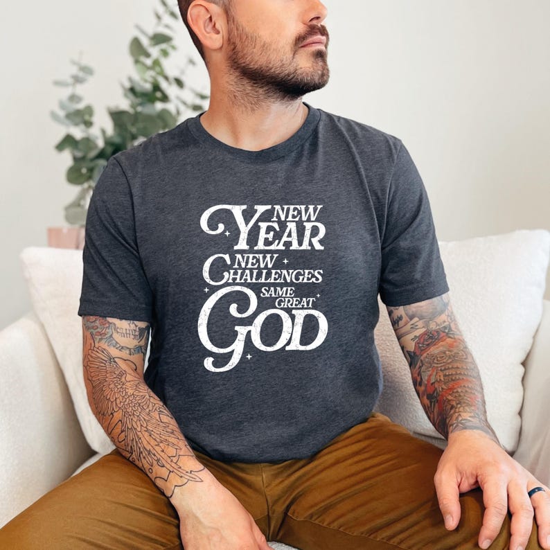 May include: A dark grey t-shirt with a white graphic that reads "New Year New Challenges Same Great God".
