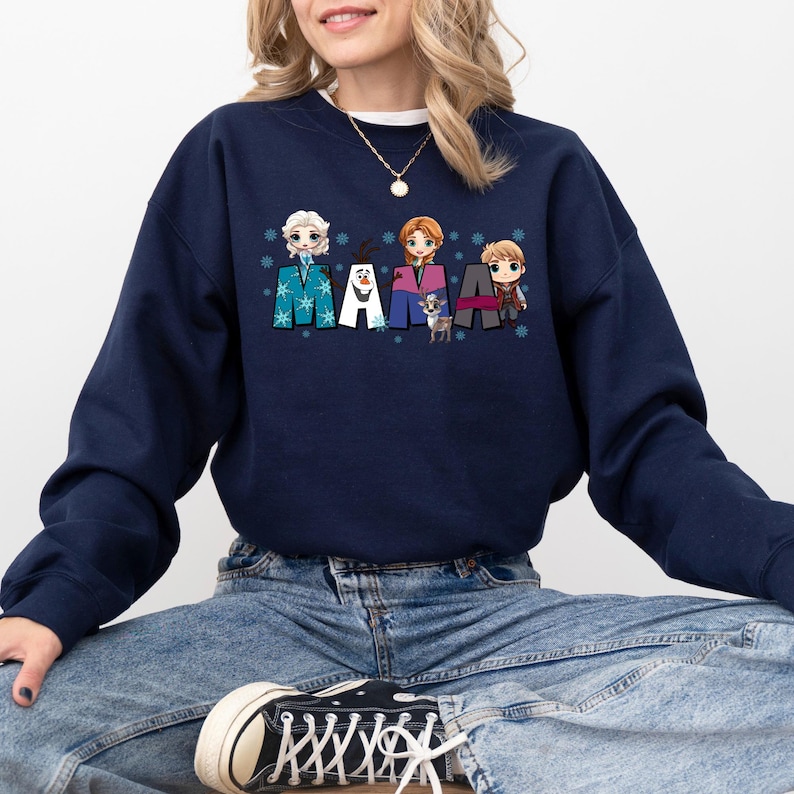 Puede incluir: Una sudadera azul marino con un gr&aacute;fico de personajes de dibujos animados de la pel&iacute;cula Frozen. Los personajes est&aacute;n dispuestos para deletrear la palabra "MAMA" con copos de nieve en el fondo.