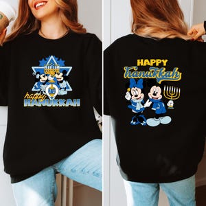 May include: Black sweatshirt with a graphic of Mickey Mouse and Minnie Mouse dressed in blue and white, holding a dreidel and a menorah. The text "Happy Hanukkah" is written in yellow on the sweatshirt.