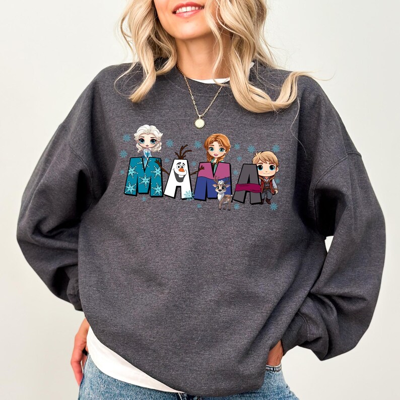 Puede incluir: Una sudadera gris oscuro con un estampado gr&aacute;fico de la palabra "MAMA" con personajes de dibujos animados de la pel&iacute;cula Frozen. Los personajes incluyen a Elsa, Anna, Olaf y Kristoff.