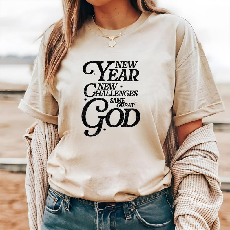 May include: A beige t-shirt with a black graphic that reads "New Year New Challenges Same Great God".
