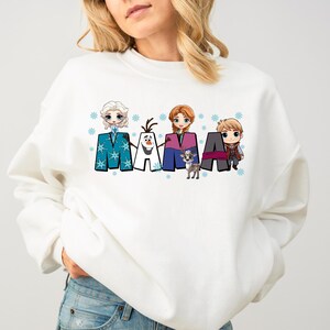 Puede incluir: Sudadera blanca con un estampado gr&aacute;fico de los personajes de la pel&iacute;cula Frozen, incluyendo Elsa, Anna, Olaf, Kristoff y Sven. El gr&aacute;fico dice "MAMA" con cada personaje de pie sobre una letra.